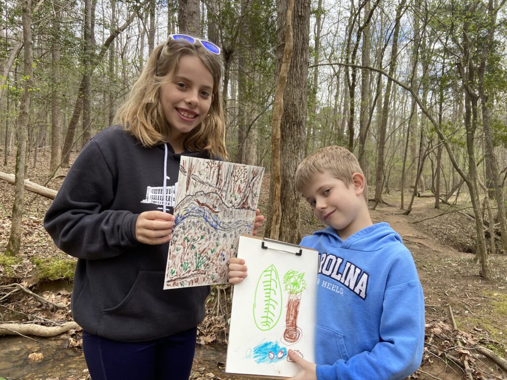 Ryan's daughter and son holding up drawings representing the scenery from an Eno River trail.