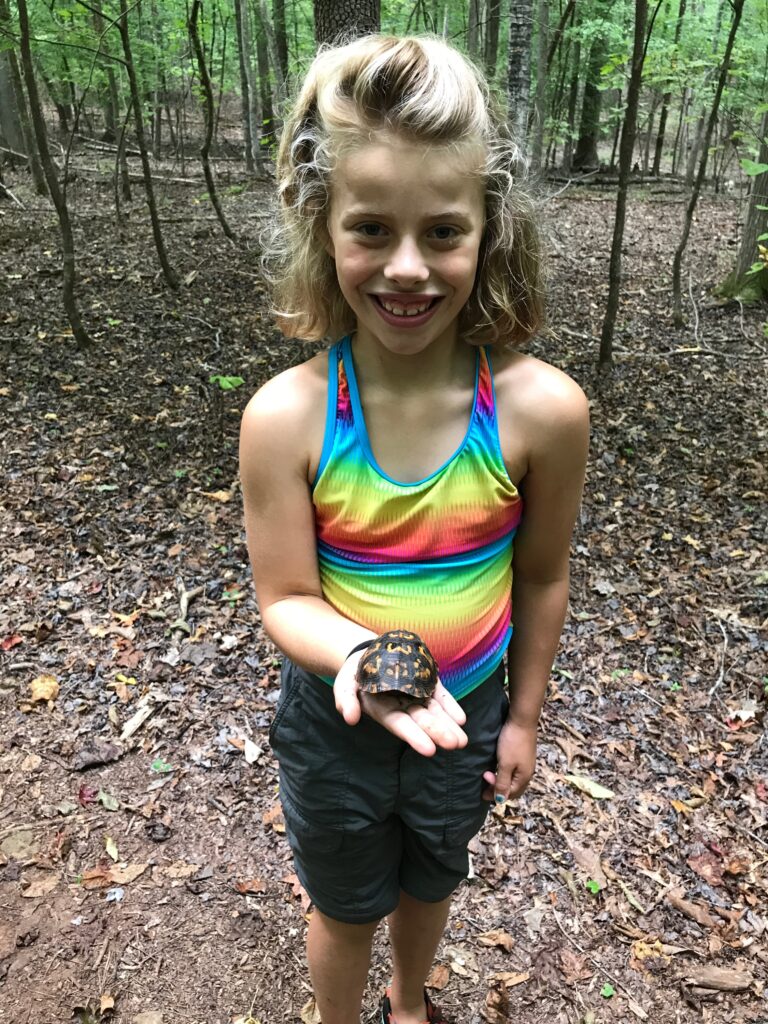 Ryan's daughter as an older child smiling while holding a small box turtle in the palm of her hand.